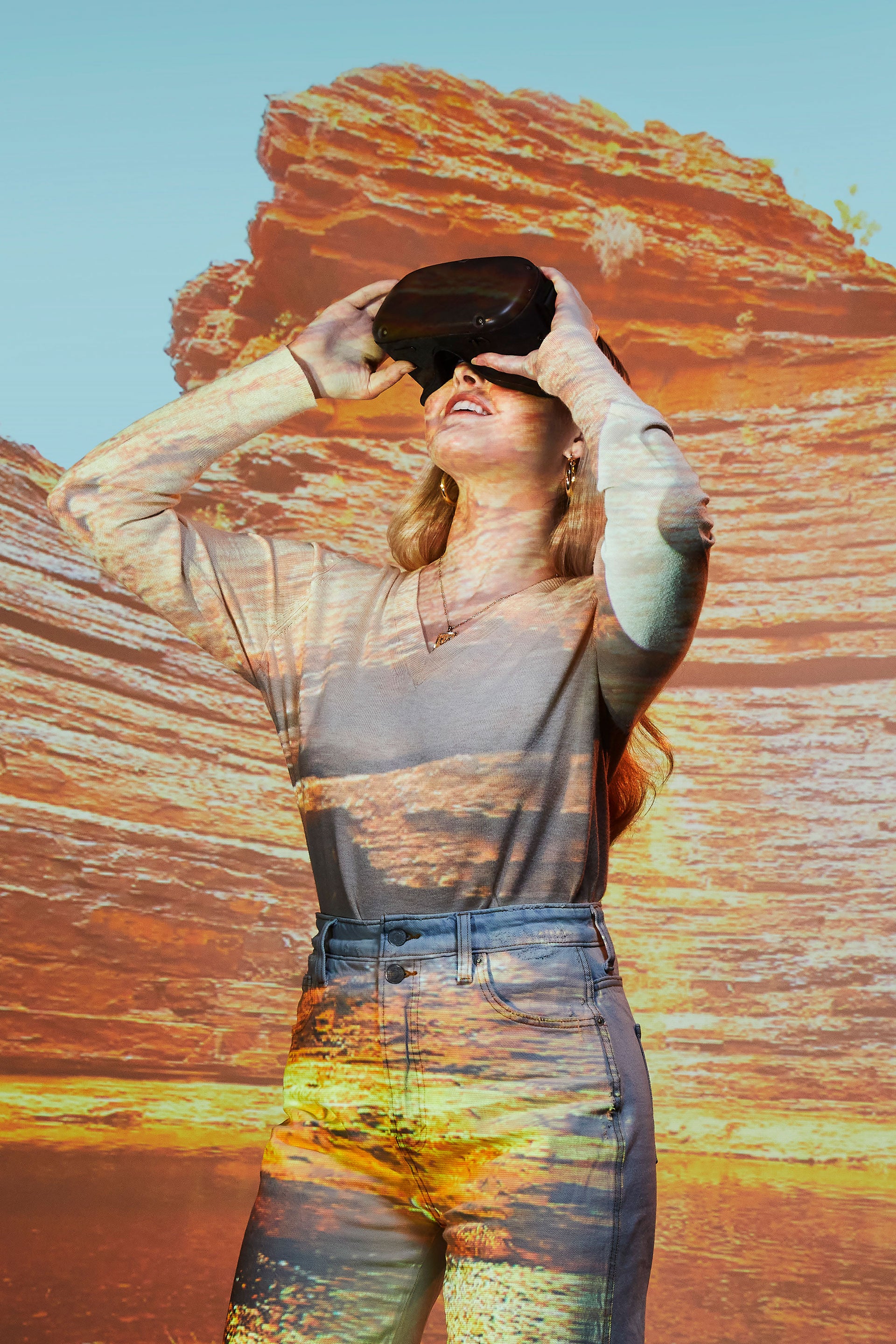 female wearing a VR headset looking up while standing in front of a digital projection of a canyon wall