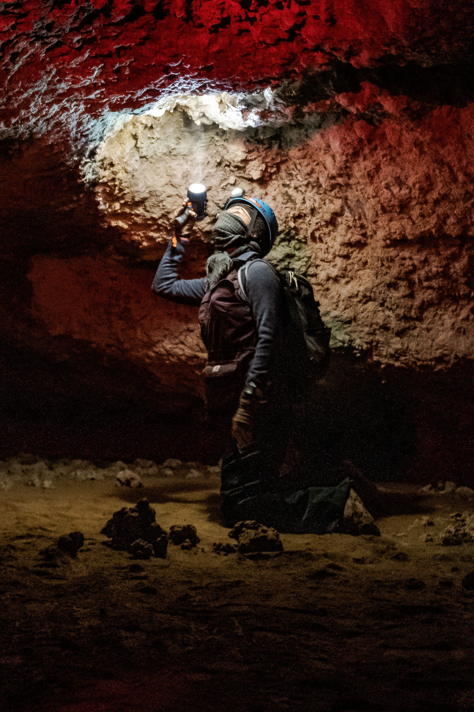 A person kneeling in a dark cave pointing a flashlight at the ceiling